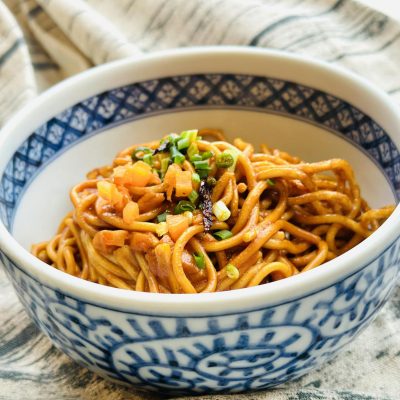 A bowl of homemade vegetable noodles garnished with fresh scallions and herbs.