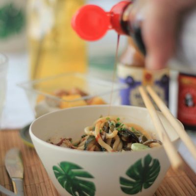 A flavorful bowl of noodles with sauce being poured, garnished with vegetables.